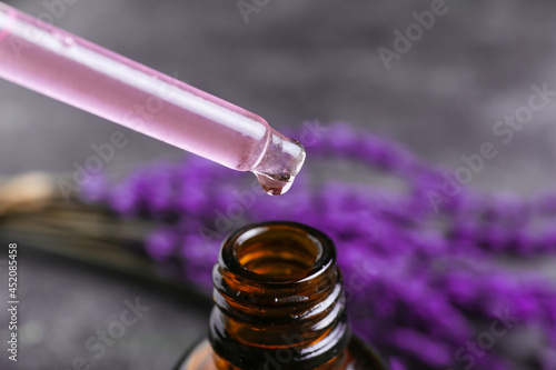 Dripping of lavender essential oil into bottle on dark background