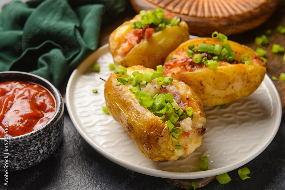 Plate with baked potato and sauce on dark background