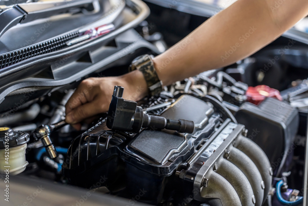 Close up spark plug coil on engine cover and a man use block wrench remove a bolt for take off coil engine service in garage and engine room background Close up spark plug coil on engine cover and a man use block wrench remove a bolt for take off coil engine service in garage and engine room background