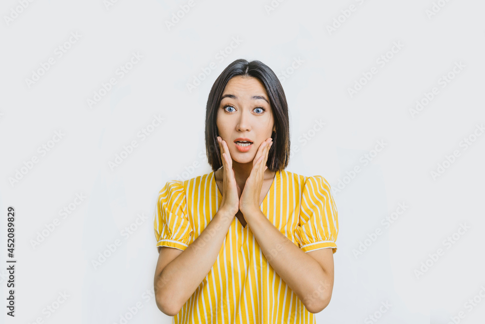 asian girl is surprised with her mouth open. a young Asian woman in a yellow shirt on a white background is confused and surprised asian girl is surprised with her mouth open. a young Asian woman in a yellow shirt on a white background is confused and surprised