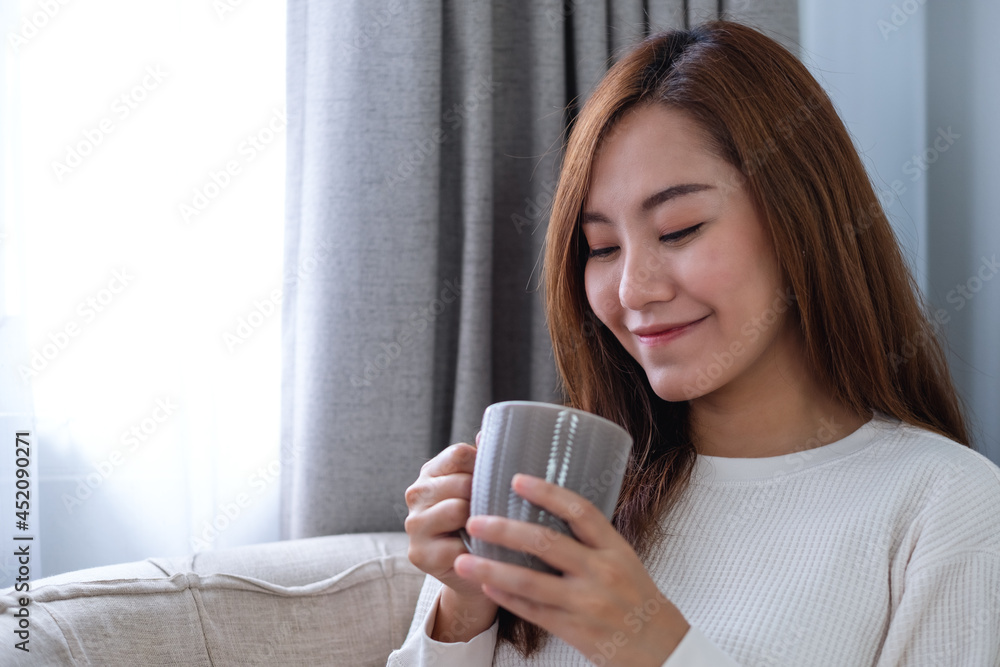 Portrait image of a beautiful asian woman drinking hot coffee and relaxing on a sofa at home Portrait image of a beautiful asian woman drinking hot coffee and relaxing on a sofa at home