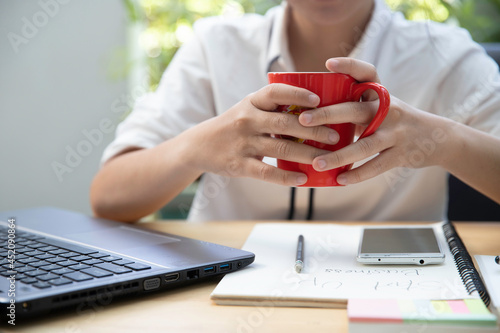 The hand of a businesswoman is lifting a cup of coffee on the table with laptop computer on workplace. photo