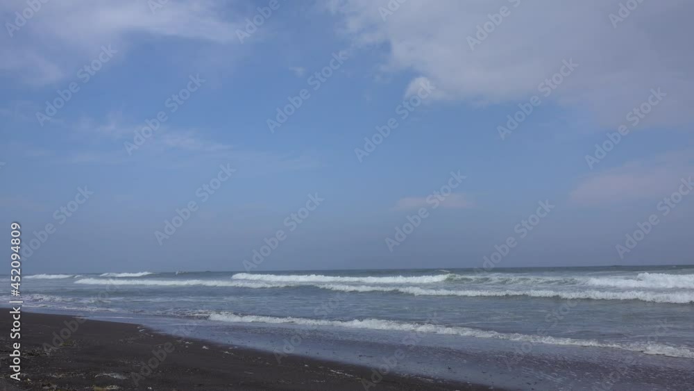 Turquoise surf waves roll one after another. Foam on the unique black sand of the beach. Clouds in a blue sky. Khalaktyrsky Beach. The Pacific Ocean. Kamchatka. Turquoise surf waves roll one after another. Foam on the unique black sand of the beach. Clouds in a blue sky. Khalaktyrsky Beach. The Pacific Ocean. Kamchatka.