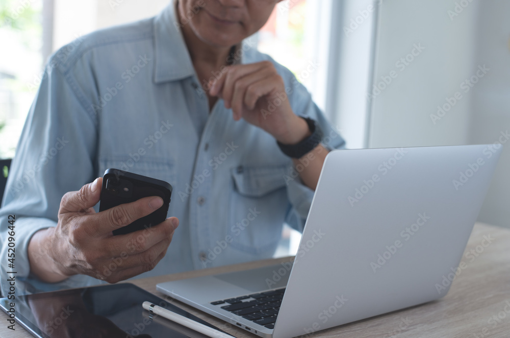 Asian business man using mobile phone, thinking about his work project during working on laptop computer with digital tablet on table at home office Asian business man using mobile phone, thinking about his work project during working on laptop computer with digital tablet on table at home office