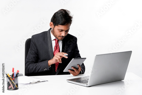 Young indian man in suit and using tablet and laptop at office