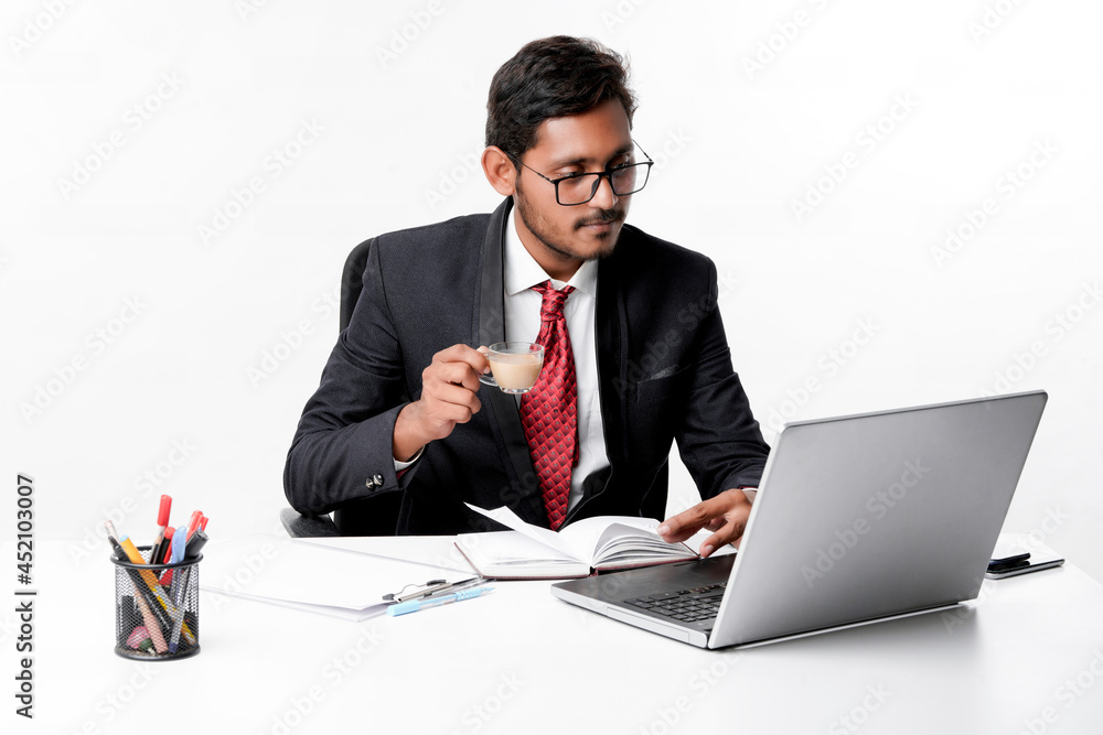 Young indian businessman working on laptop and drinking tea at o Young indian businessman working on laptop and drinking tea at o