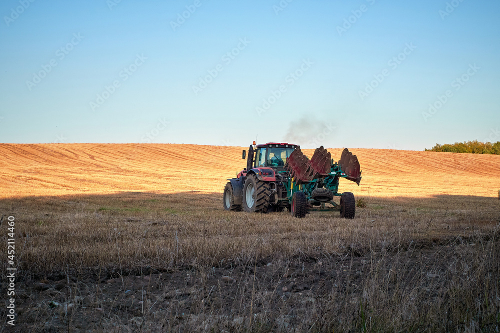 Fototapeta premium Agricultural work. Tractor with a plow on a summer field during the day