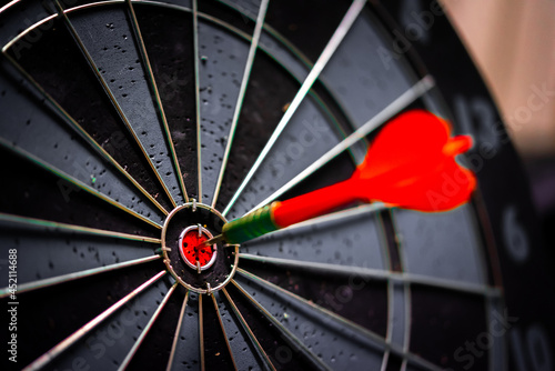 Close up shot of the dart arrow hit on bulleyes of dartboard to represent that the business reached the target of company with dark tone picture style. Target and goal as concept. 