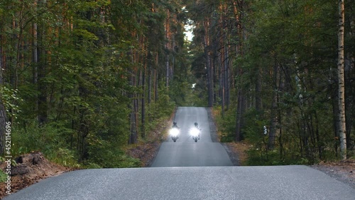 Motor riding - two women in helmets riding on empty road in the woods with turned on headlights