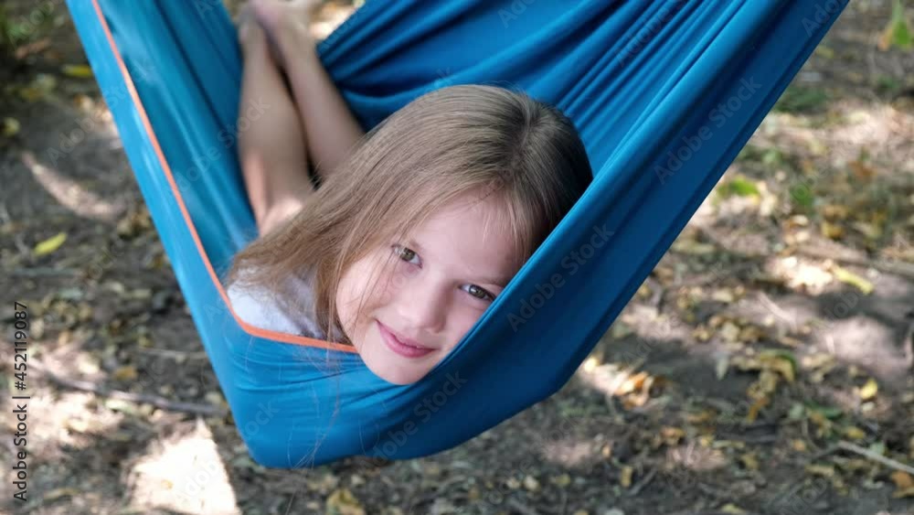 Portrait of a little blond caucasian girl lying in a blue hammock outdoors on a sunny day. Vacation for children, rest and relaxation Portrait of a little blond caucasian girl lying in a blue hammock outdoors on a sunny day. Vacation for children, rest and relaxation