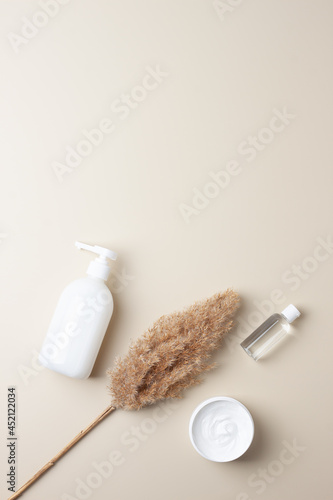 Cosmetic skin care products with pampas on pastel beige background. Flat lay, copy space
