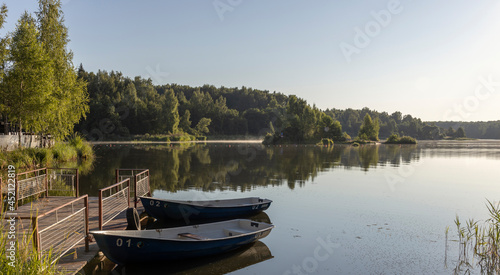 Dawn. The first rays of the sun illuminate the grass and trees on the river bank. Early morning, boats. Landscape with boats at the pier. © Sergei