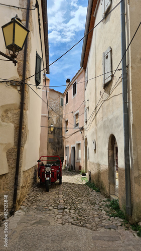 Street of an old medieval town with a red vintage motorcycle and a lantern on the wall in southern Europe
