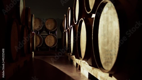 Aged wooden barrels with a wine , brandy or whiskey in a big warehouse . Dolly , gimbal movement a long row of wine barrels at a vintage winery with alcohol . Wine preparation and fermenting process