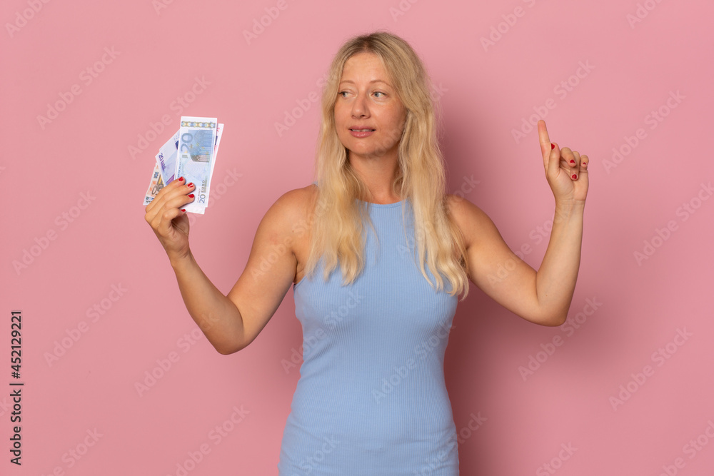 Portrait of a cheerful young woman holding money banknotes pointing finger up isolated over pink background. Portrait of a cheerful young woman holding money banknotes pointing finger up isolated over pink background.