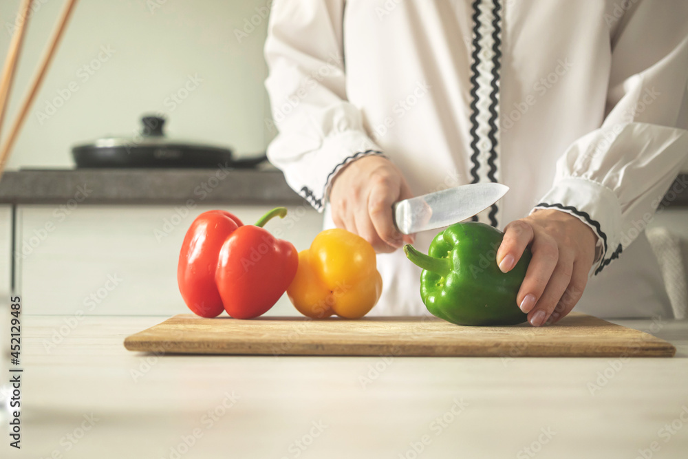 Chef slicing sweet pepper on wooden board, modern kitchen background. Woman chef cooking with ripe vegetable. healthy food concept photo Chef slicing sweet pepper on wooden board, modern kitchen background. Woman chef cooking with ripe vegetable. healthy food concept photo