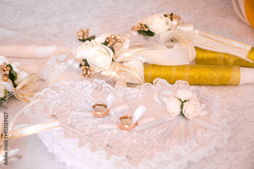 Bridal wedding rings on a white pillow in the shape of a heart. Wedding candles in gold color