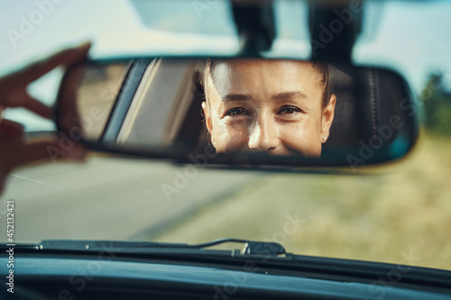 Happy woman looking at her face in rear-view mirror