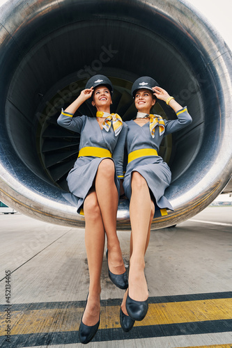 Fotografie Beautiful stewardesses in uniforms sitting cross-legged inside the turbofan engi