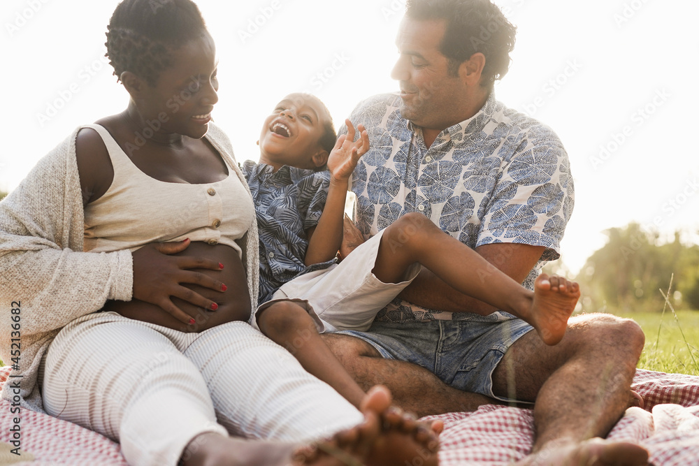 Multiracial family having fun outdoor sitting on grass - Multiethnic couple laughing together with their son - Love concept - Focus on father face