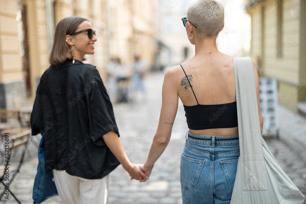 Stylish lesbian couple walking the street and holding hands together. Street fashion and lifestyle, homosexual relations