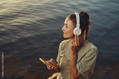 Female pressing headphones closer while enjoying music in nature