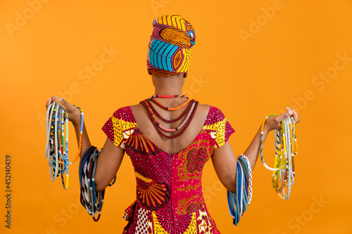 The African woman is dressed in national clothes and turned her back to the camera. She has a lot of beaded necklaces.