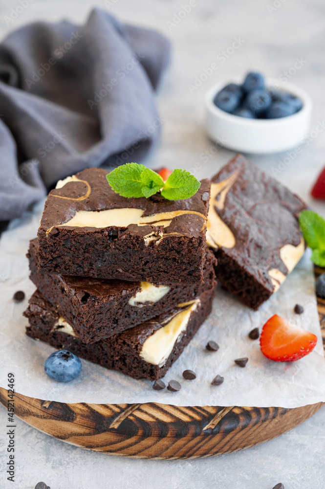 Delicious chocolate brownie cheesecake with fresh berries and mint on a wooden board on a gray concrete background. Copy space. Delicious chocolate brownie cheesecake with fresh berries and mint on a wooden board on a gray concrete background. Copy space.