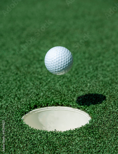An golf ball about to fall into the hole of a green. Hole in one image.