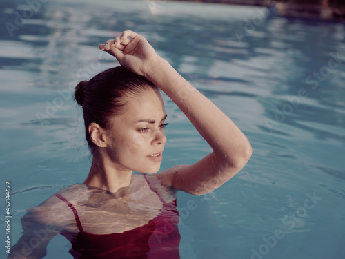 pretty woman in a swimsuit in the pool holds her hand on her head luxury attractive look