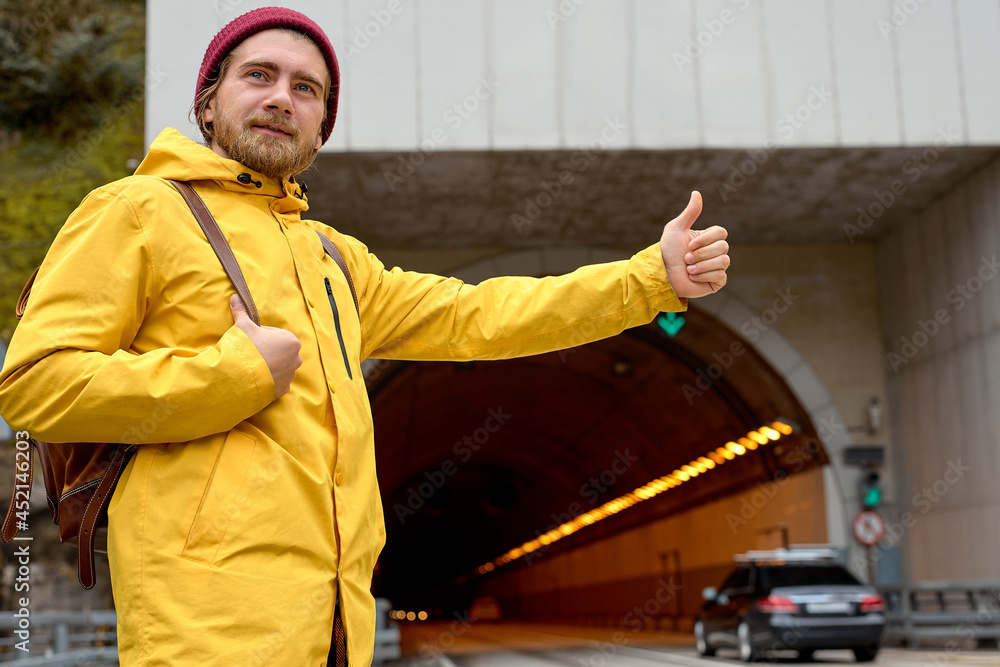 road trip, travel, gesture and people concept. caucasian young man hitchhiking and stopping car with thumbs up gesture at countryside, in yellow coat road trip, travel, gesture and people concept. caucasian young man hitchhiking and stopping car with thumbs up gesture at countryside, in yellow coat