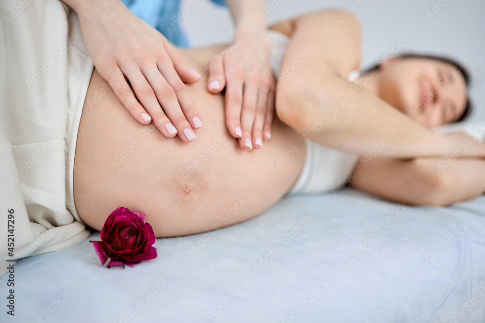 Young pregnant woman lying on couch receiving belly massage, relaxing, having rest.side view of asian female enjoying with eyes closed, focus on tummy Young pregnant woman lying on couch receiving belly massage, relaxing, having rest.side view of asian female enjoying with eyes closed, focus on tummy