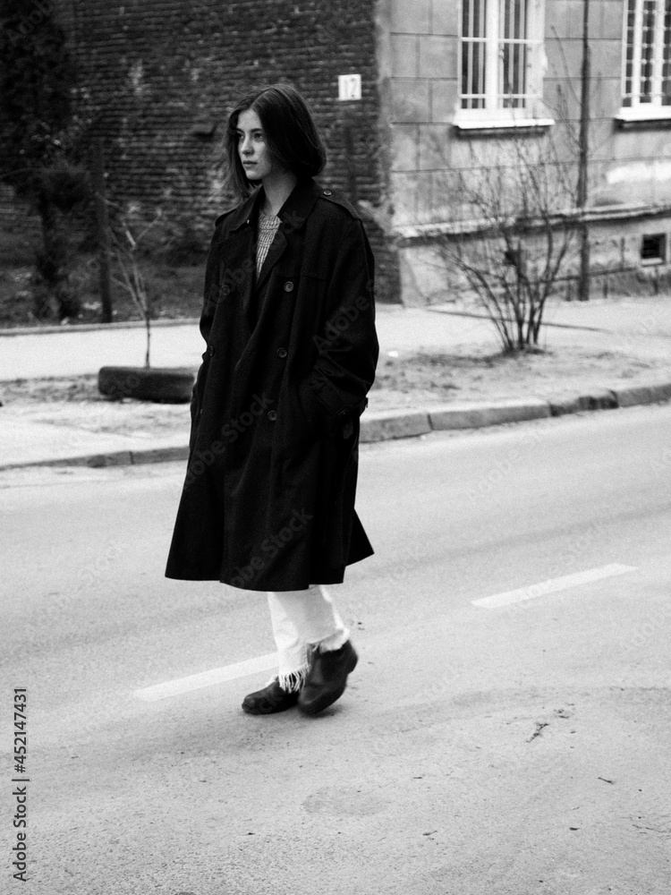 Beautiful young woman in the dark coat walking on the city street, monochrome. 
