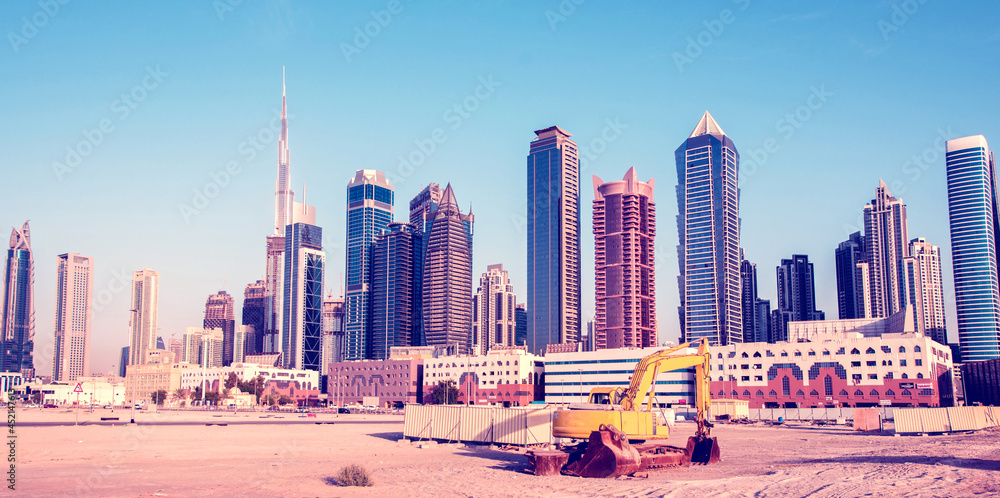 Bulldozer on the sand against the backdrop of skyscrapers in Dubai as a symbol of UAE development.