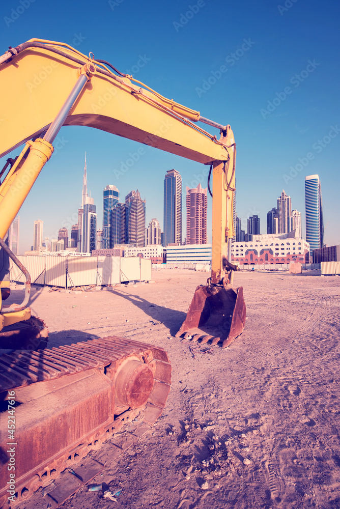 Bulldozer on the sand against the backdrop of skyscrapers in Dubai as a symbol of UAE development