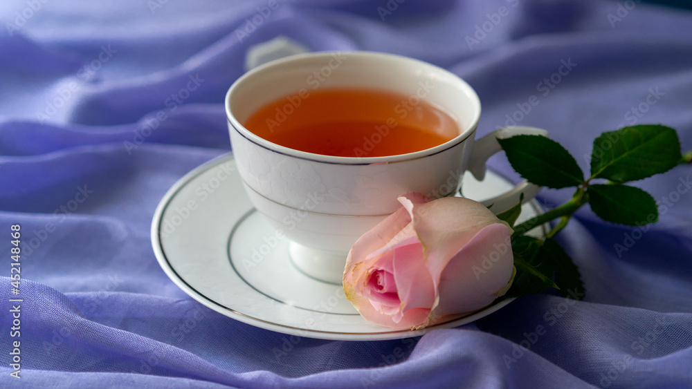 A cup of tea and a pink rose on a purple background. Romantic, sweet, dating concept. A cup of tea and a pink rose on a purple background. Romantic, sweet, dating concept.