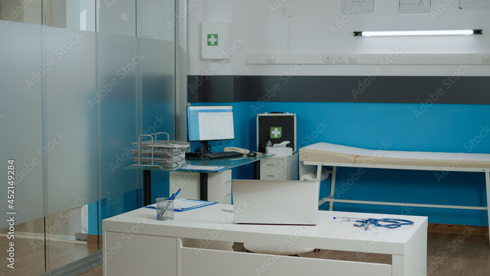 Empty doctors office with medical instruments at facility for healthcare treatment. Nobody in cabinet room for health specialist designed with desk, laptop, computer, bed and stethoscope Empty doctors office with medical instruments at facility for healthcare treatment. Nobody in cabinet room for health specialist designed with desk, laptop, computer, bed and stethoscope