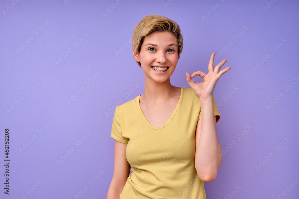 Short-haired Female showing ok gesture, everything will be OK. Isolated purple studio background. Young caucasian lady in casual yellow tshirt posing, smiling. Human emotions, people lifestyle Short-haired Female showing ok gesture, everything will be OK. Isolated purple studio background. Young caucasian lady in casual yellow tshirt posing, smiling. Human emotions, people lifestyle
