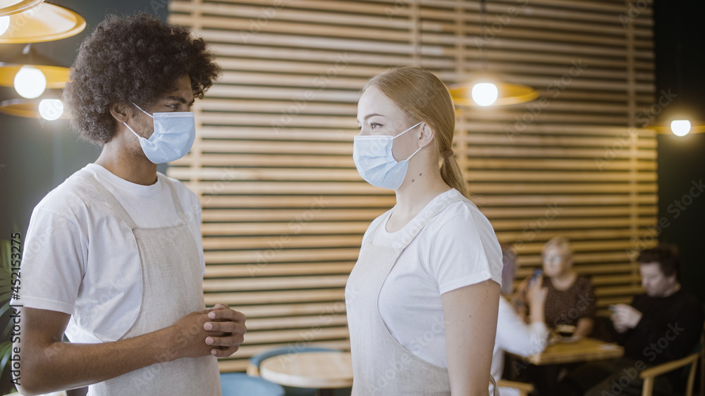 Obraz premium Waiters wearing face masks at work, cafe during pandemic guests sitting at table