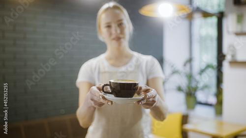 Female barista holding out coffee cup to customer, morning tradition, business