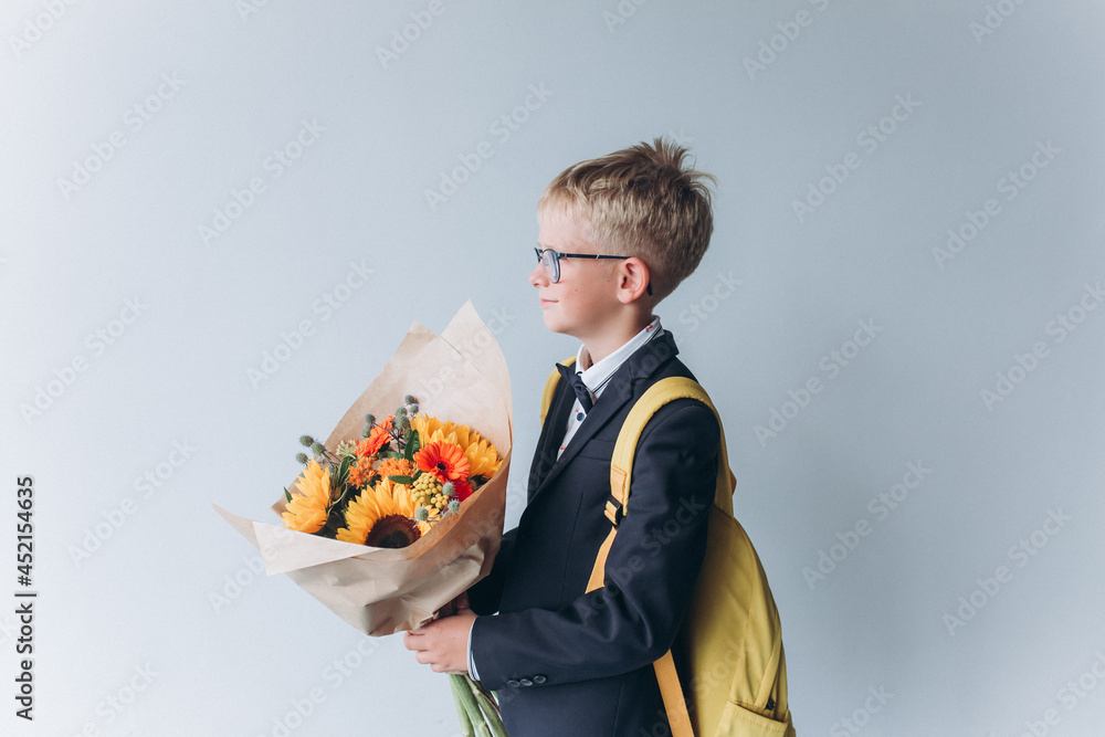 School boy in eyeglasses with bouquet of flowers with back pack on isolated grey background School boy in eyeglasses with bouquet of flowers with back pack on isolated grey background