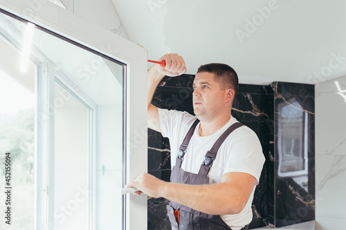 The worker adjusts the window in the apartment of the house after repair