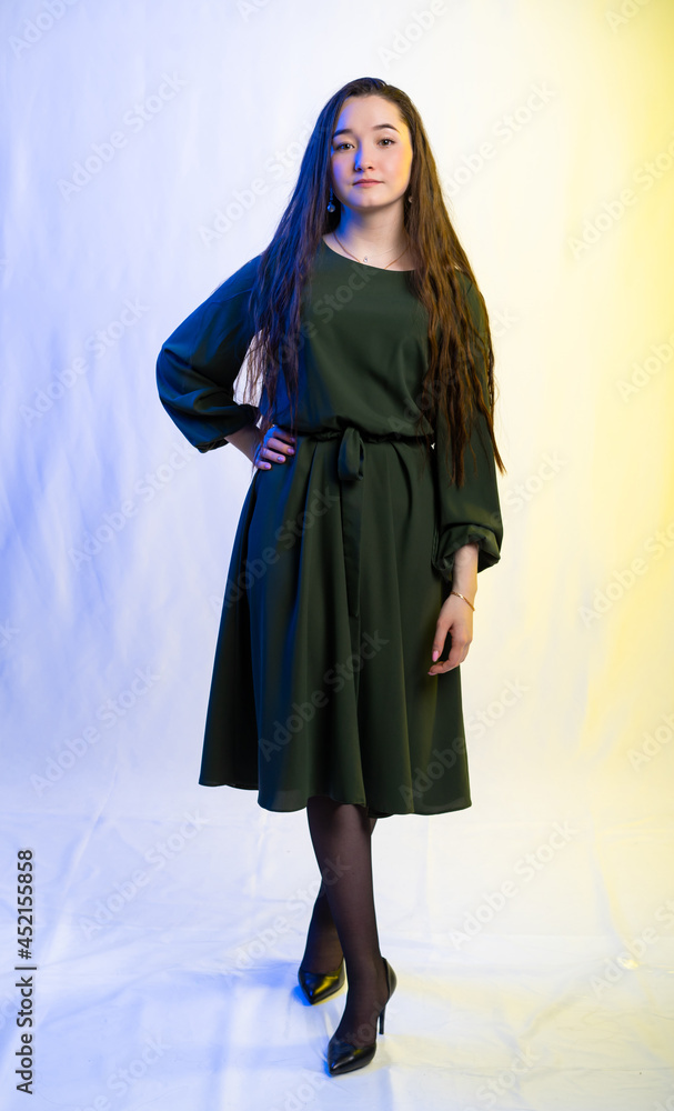 Fototapeta premium full-length portrait of a girl. model in a green dress, black shoes. long curly hair. colored background.