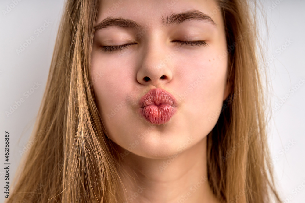 Close-up portrait of young girl kissing with eyes closed, isolated on white background. Attractive female with natural long brown hair with perfect skin in love, kiss at camera. people concept Close-up portrait of young girl kissing with eyes closed, isolated on white background. Attractive female with natural long brown hair with perfect skin in love, kiss at camera. people concept