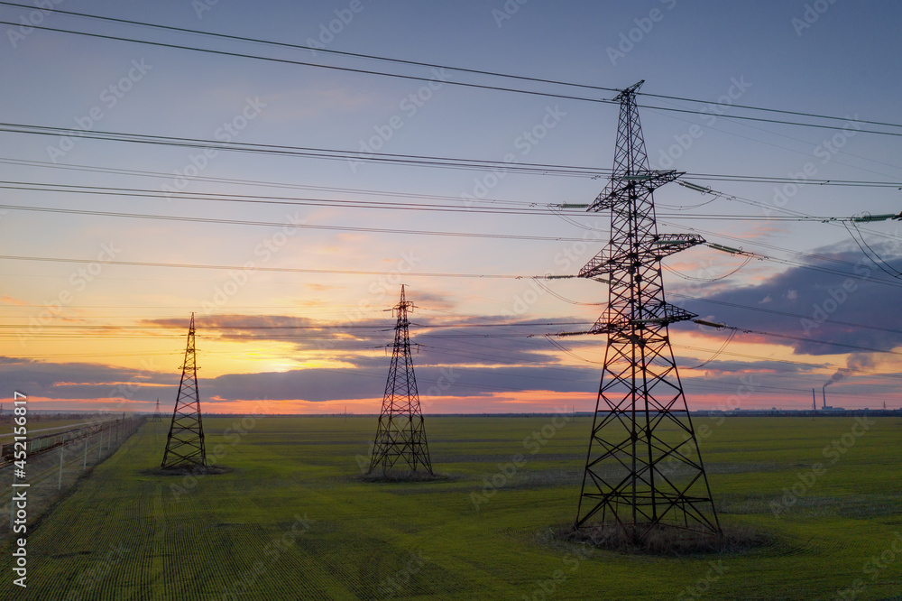 high voltage lines and power pylons in a green agricultural field against a saturated sunset sky
