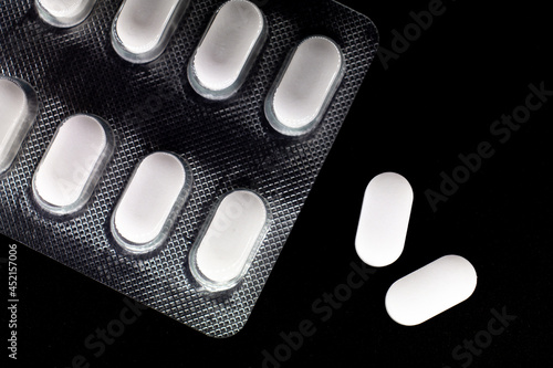 white, oval tablets in a blister on a black background. macro photo