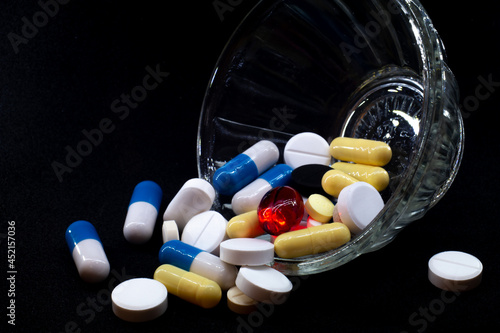 pills of different shapes and colors on a black background in a glass bowl. macro photo