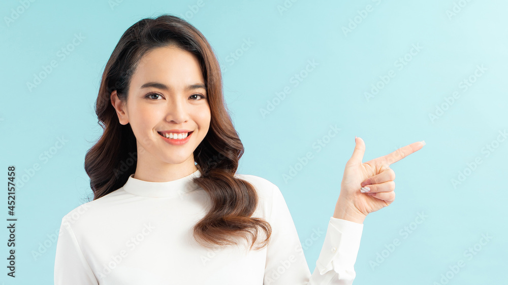 Smiling woman pointing finger side. Isolated portrait on blue. Smiling woman pointing finger side. Isolated portrait on blue.