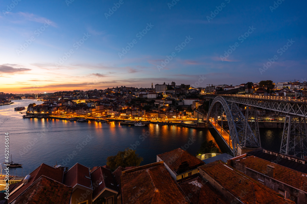 Delightful panoramic night view of the city of Porto and illuminated banks of the Douro river. The red tiled roofs of Vila Nova de Gaia are visible in the foreground. One of the famous world landmarks