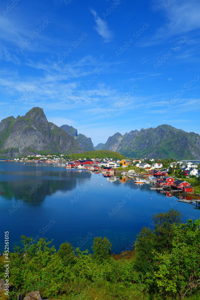 Reine in Lofoten Islands, Norway, with traditional red rorbu huts under blue sky with clouds.